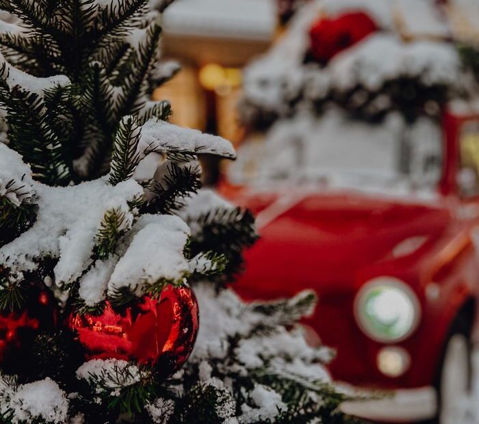 A festive winter scene featuring a snowy Christmas tree with baubles and a decorated vintage car in the background.