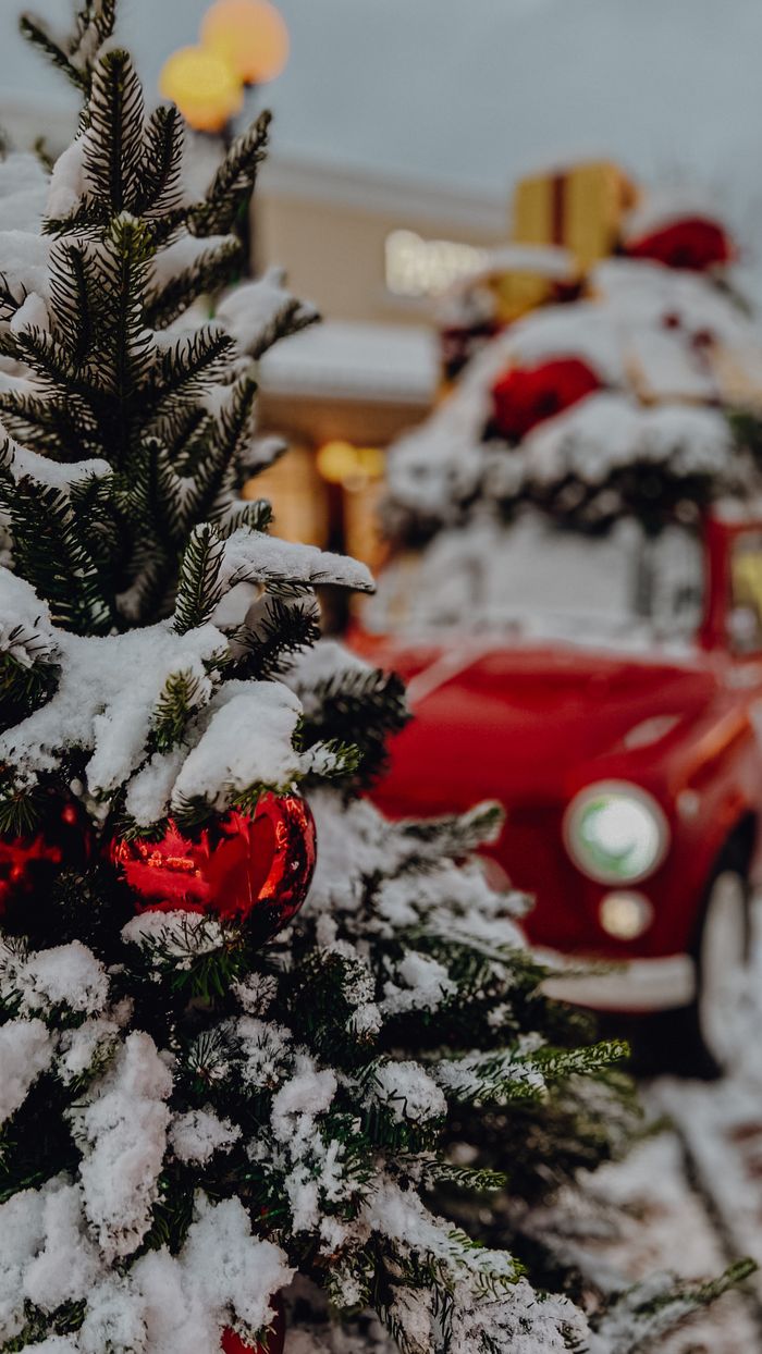 A festive winter scene featuring a snowy Christmas tree with baubles and a decorated vintage car in the background.